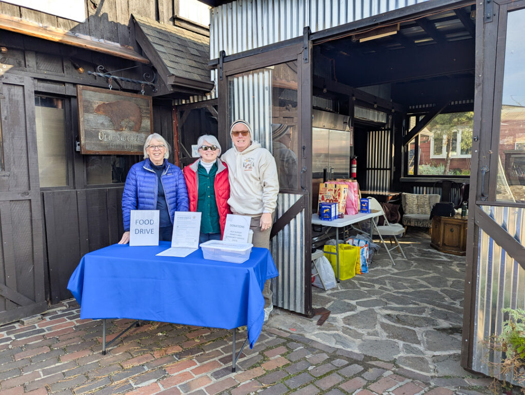 three volunteers at Oso Sweet managing the table where food was collected for the food drive